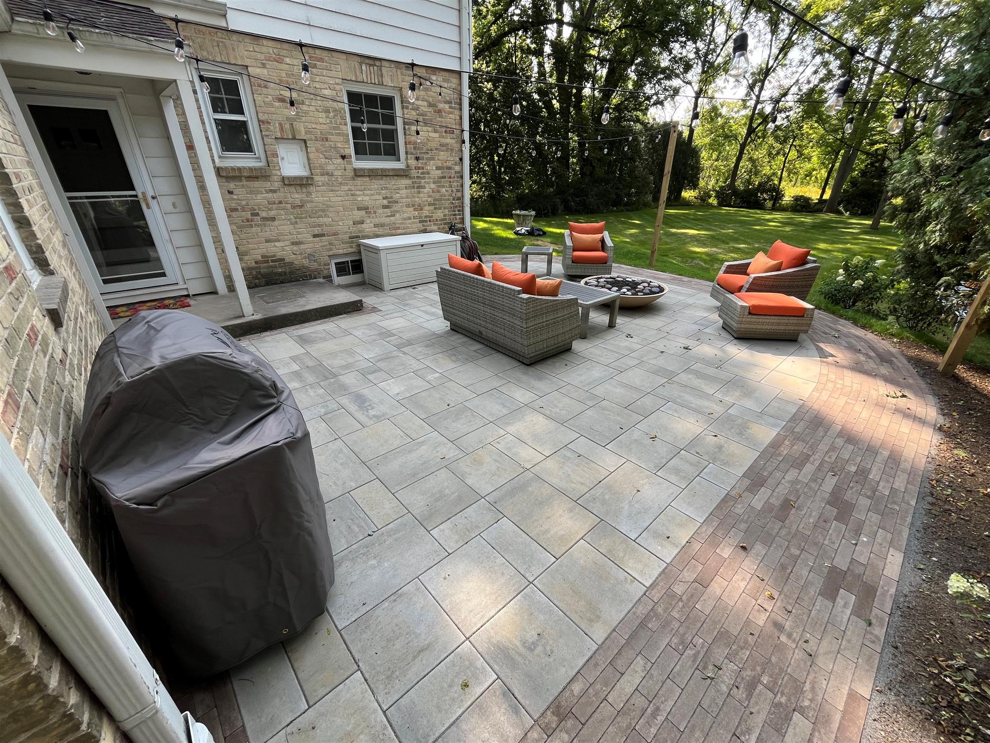 Brick patio with a small fire pit, patio furniture, string lights, and a grill