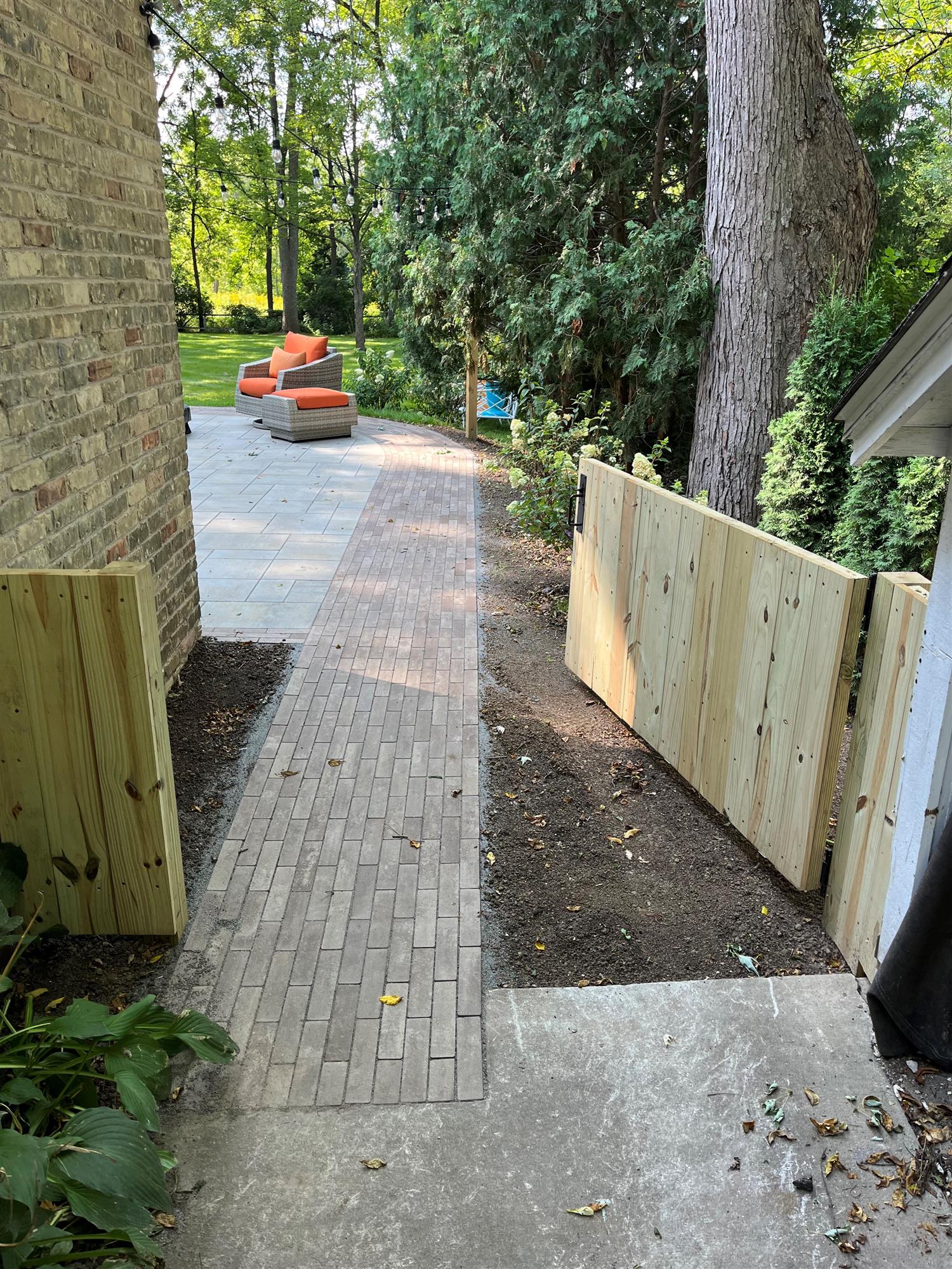 Side pathway with a wooden fence and swinging door, leading from the driveway to a backyard patio.